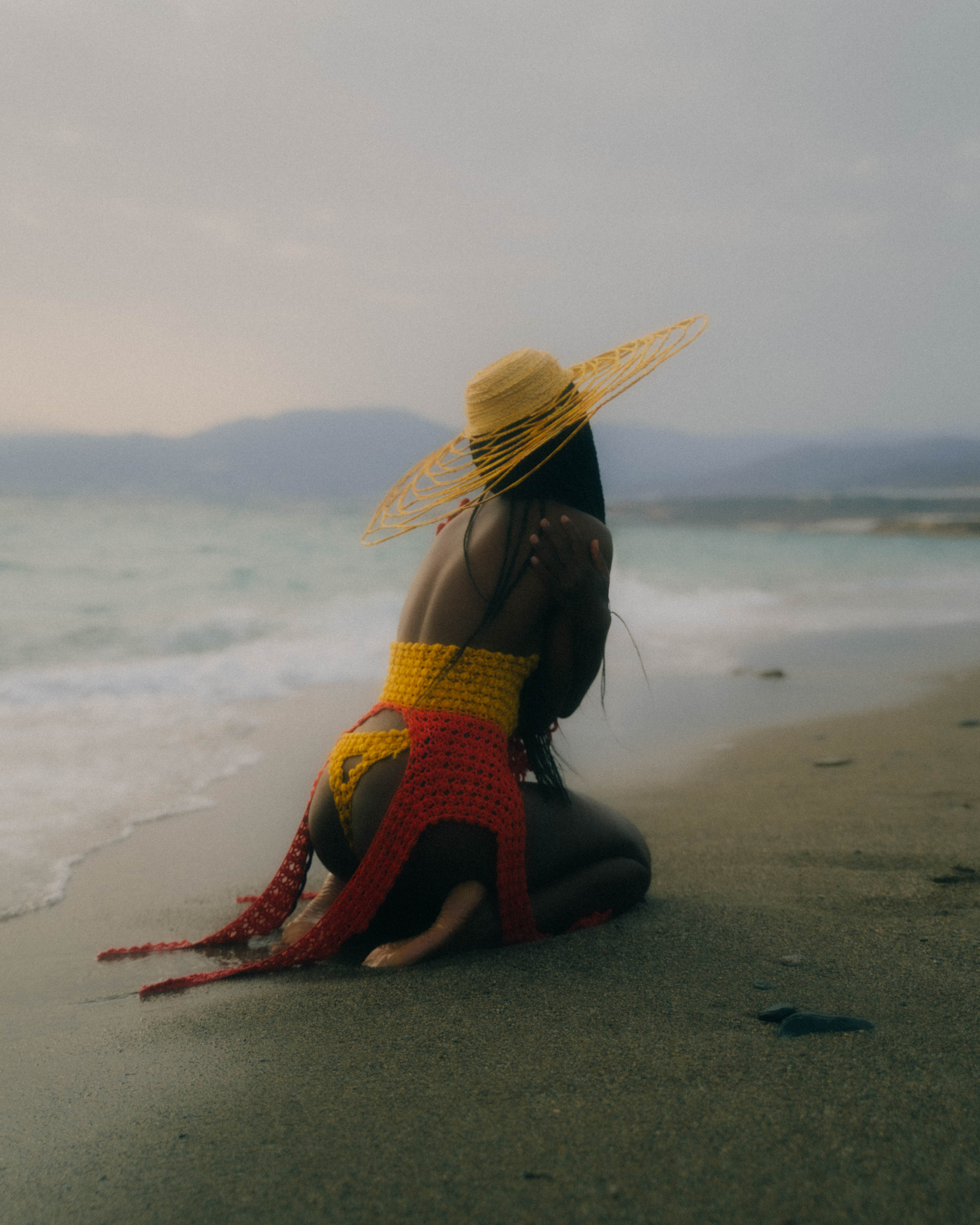 Back shot of MENIGILDA, crochet yellow and orange swim suit paired with dry-branch woven hat.