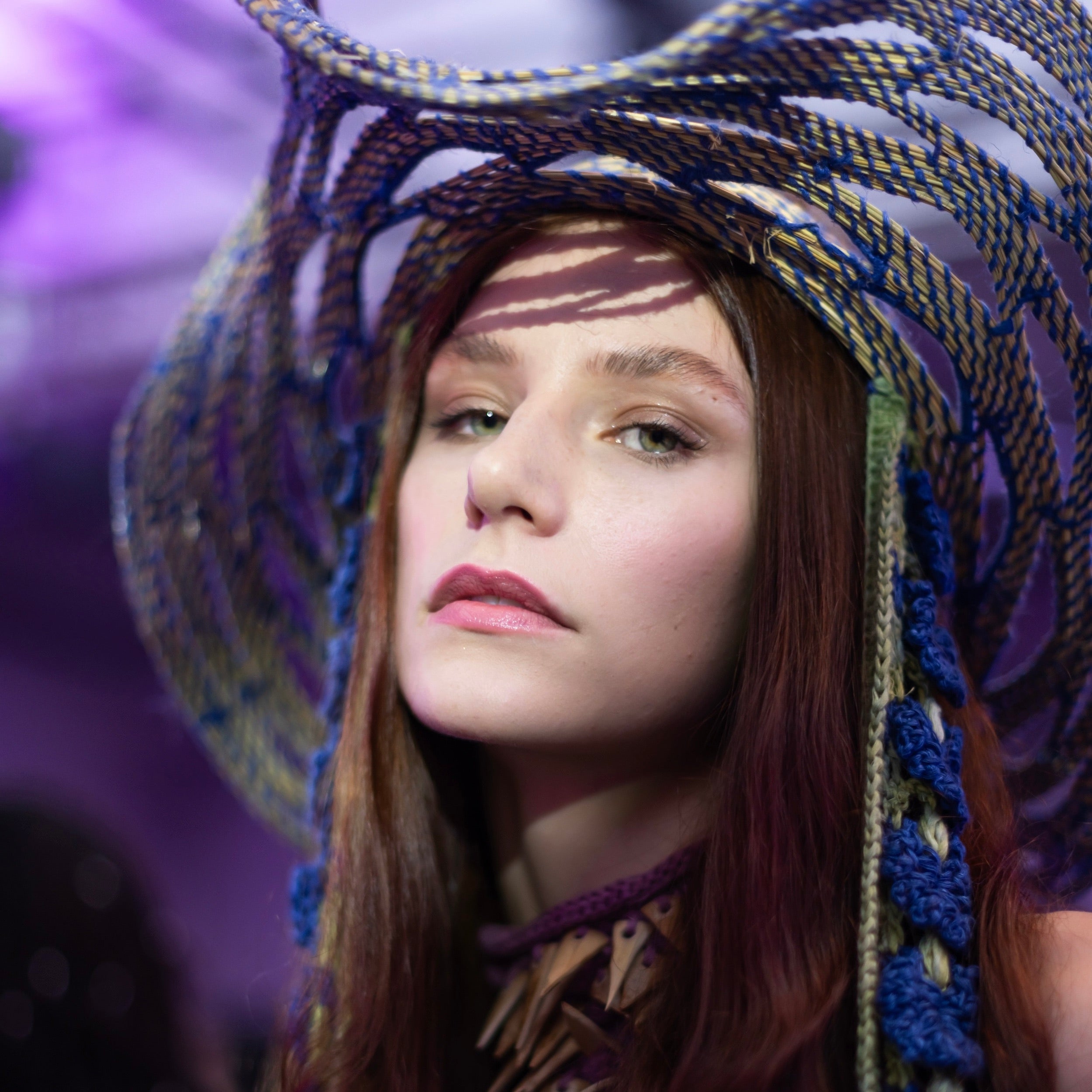 Close-up of Tina Kolodiy wearing Look 3, TABERNAS, from REGENERATIVE FOLKLORE at London Fashion Week 2023. Featured prominently is the TABERNAS hat, meticulously woven using ancestral techniques with dry branches sourced from the mountains of Southern Spain. Adorned with blue and green crocheted pineapple and tencel flower straps