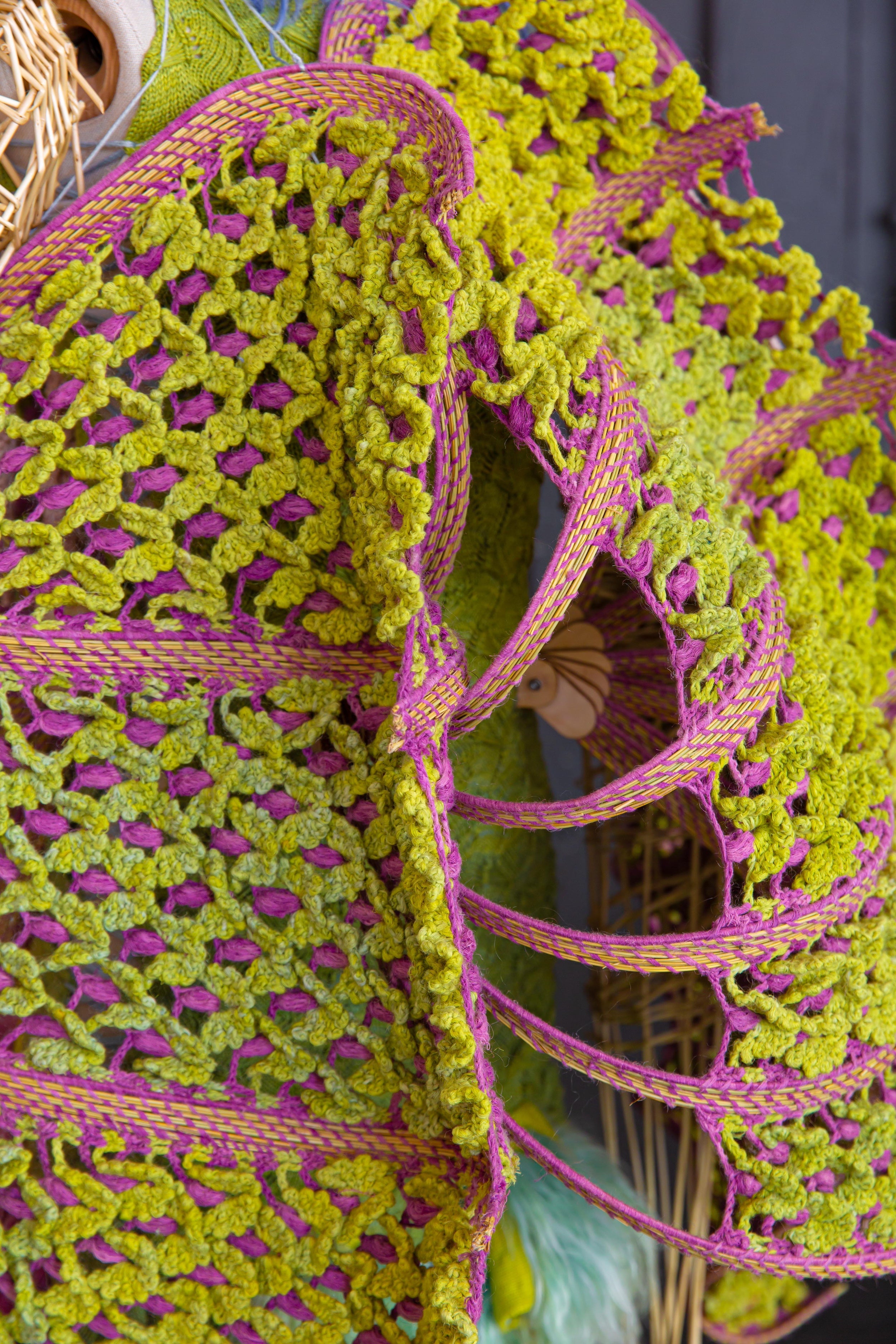 Close up of crochet structure from look 4, ABANICOS from REGENERATIVE FOLKLORE . Green and pink modular crochet structure made from nettle yarn, dyed with invasive plants and woven dry branches from Southern Spain.