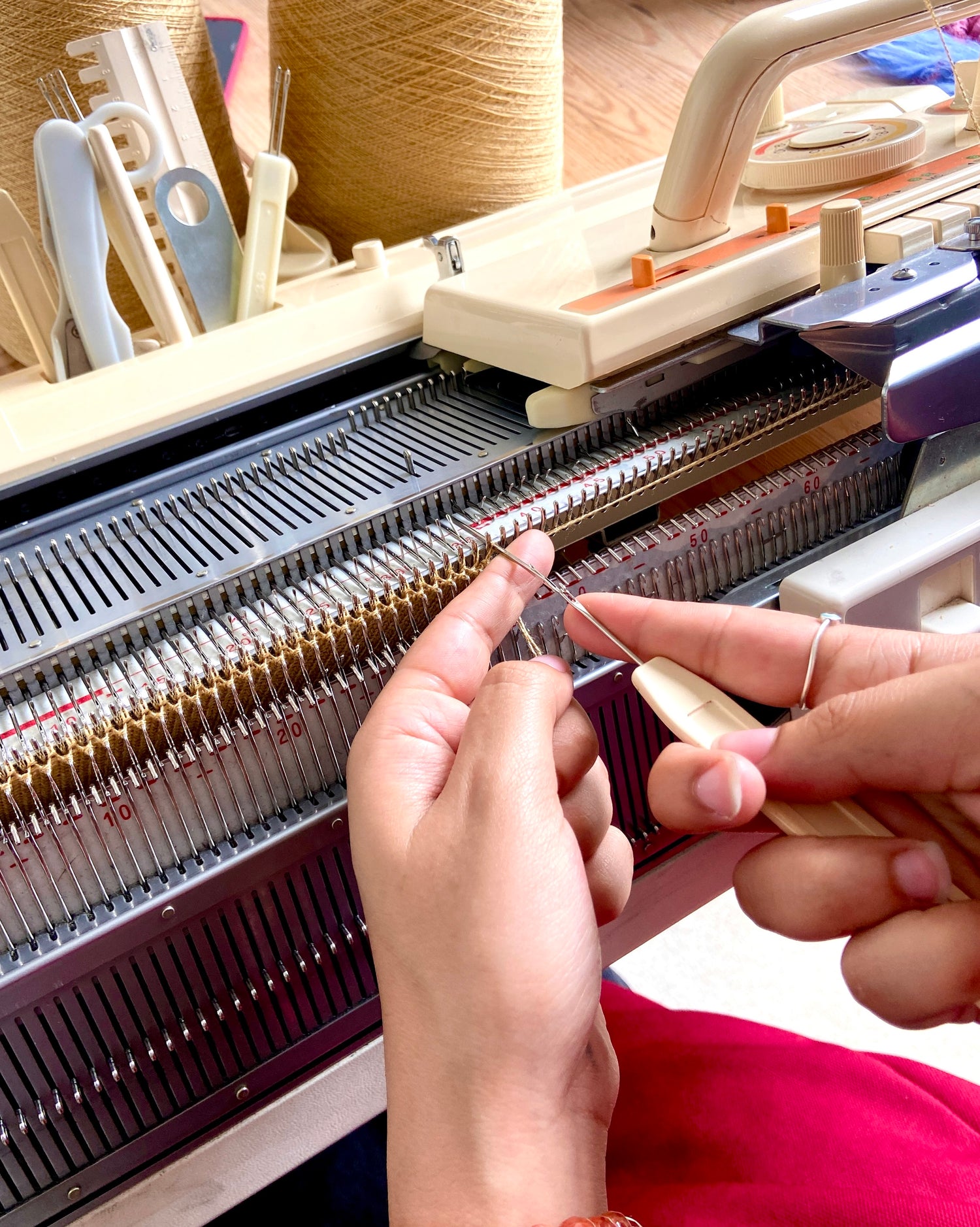 Hands in the process of transferring stitches using a transfer tool on a domestic double bed knitting machine.